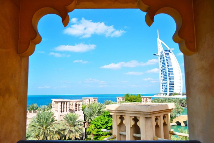 Experience the stunning views of the Burj Al Arab against a clear blue sky framed by lush greenery and architectural elegance showcasing Dubai's unmatched luxury and design.